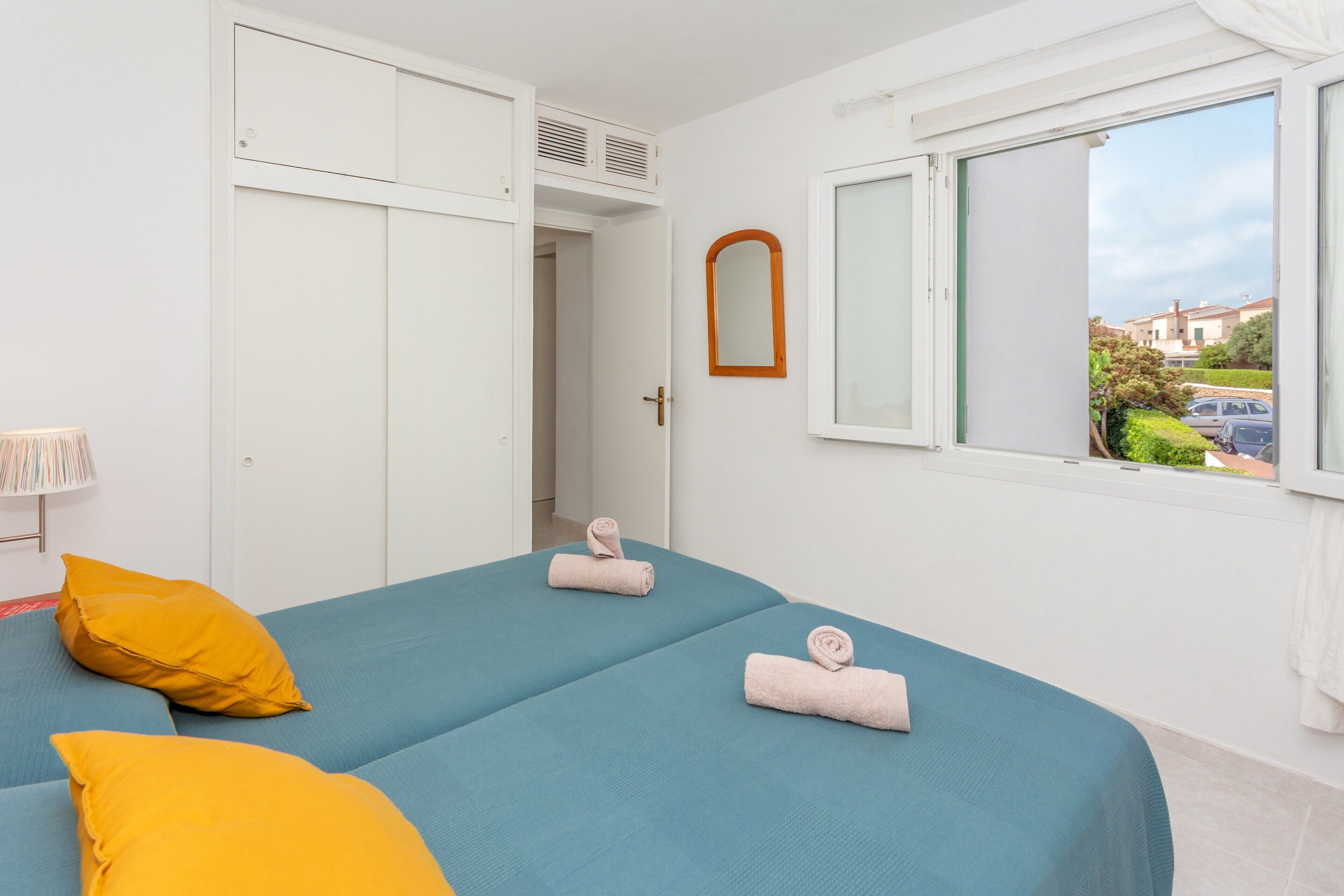 Un dormitorio con dos camas, una ventana con vistas, un espejo y una puerta que da a otra habitación.