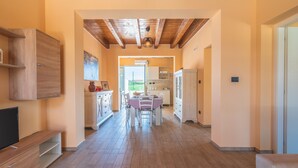 Un'ampia zona giorno con pavimento in legno, un tavolo da pranzo con sedie, un mobile TV e una cucina sullo sfondo.