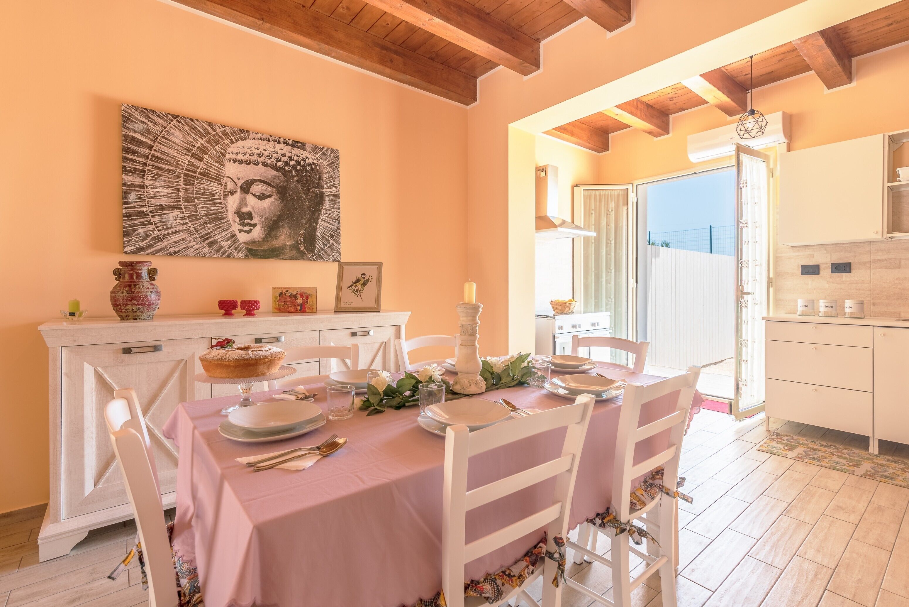 A dining area with a table set for two, a Buddha painting on the wall, and a view of the outside.