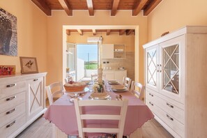 A dining area with a table set for four, a kitchen in the background, and a wooden ceiling. - Holiday Home 'Brucoli Mare 2' with Sea View, Terraces, Wi-Fi & A/C (Brucoli)