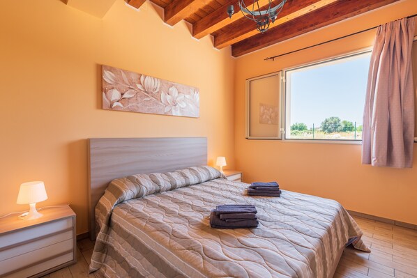 A bedroom with a bed, a nightstand, a lamp, a window with curtains, and a painting on the wall. - Holiday Home 'Brucoli Mare 2' with Sea View, Terraces, Wi-Fi & A/C (Brucoli)
