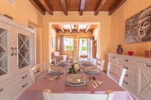 A dining room with a table set for four, white chairs, a wooden ceiling, and a Buddha painting on the wall. - Holiday Home 'Brucoli Mare 2' with Sea View, Terraces, Wi-Fi & A/C (Brucoli)