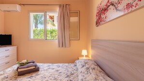 Une chambre à coucher avec un lit, une télévision, une fenêtre avec des rideaux, une lampe de chevet et un tableau au mur.