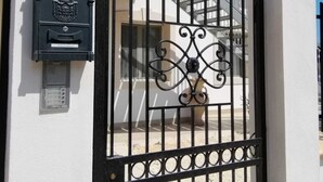 Une entrée fermée par un portail, avec une boîte aux lettres et un portail en métal décoratif.