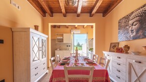 Un coin repas avec une table dressée pour quatre personnes, des meubles blancs, un tableau représentant un Bouddha et une vue sur l’extérieur par une porte ouverte.