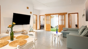Een woonkamer met een flatscreen televisie, een bank, een salontafel en een eethoek met een tafel en stoelen.