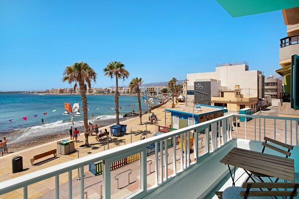 Un balcon avec vue sur la plage, les palmiers et les bâtiments.