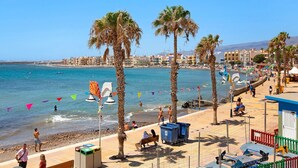 Een promenade aan het strand met palmbomen, een strand en een stadsgezicht op de achtergrond.