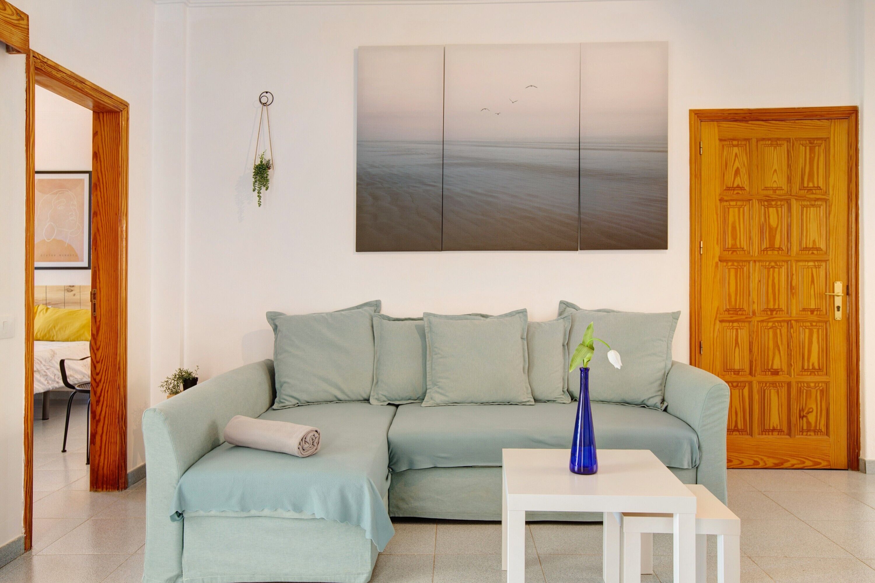 A living room with a sofa, a small table, a painting, and a wooden door.