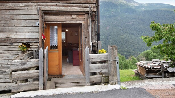 Una cabaña de madera tipo tronco con un letrero que dice 'Tawain', un porche de madera y vistas a una cadena montañosa boscosa.