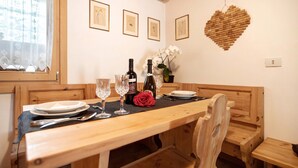 Una mesa de comedor de madera con platos, vasos y una botella, ubicada en una habitación con bancos de madera y una decoración de corazón en la pared.
