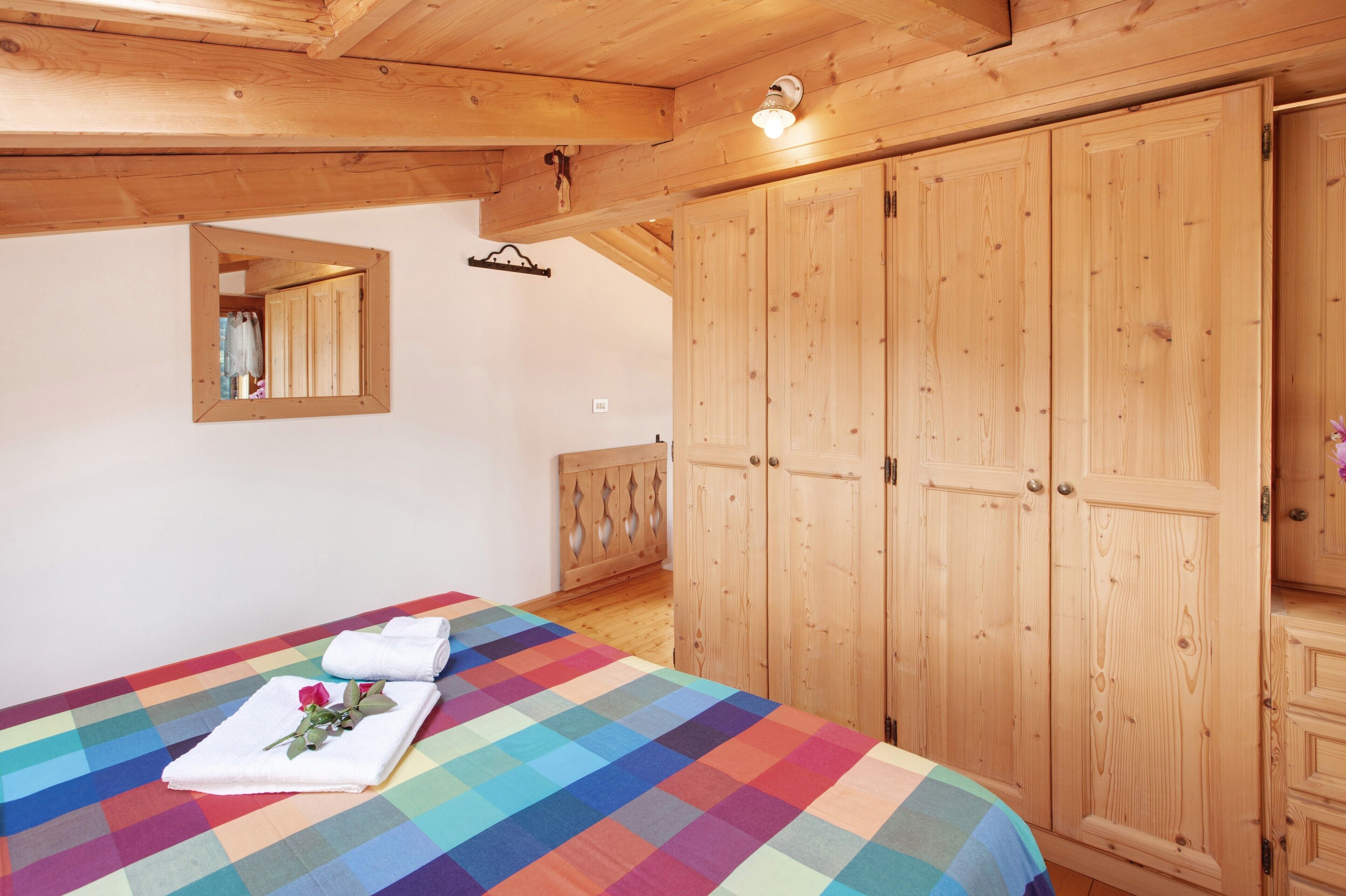 Un dormitorio con cama, un armario de madera y un espejo en la pared.