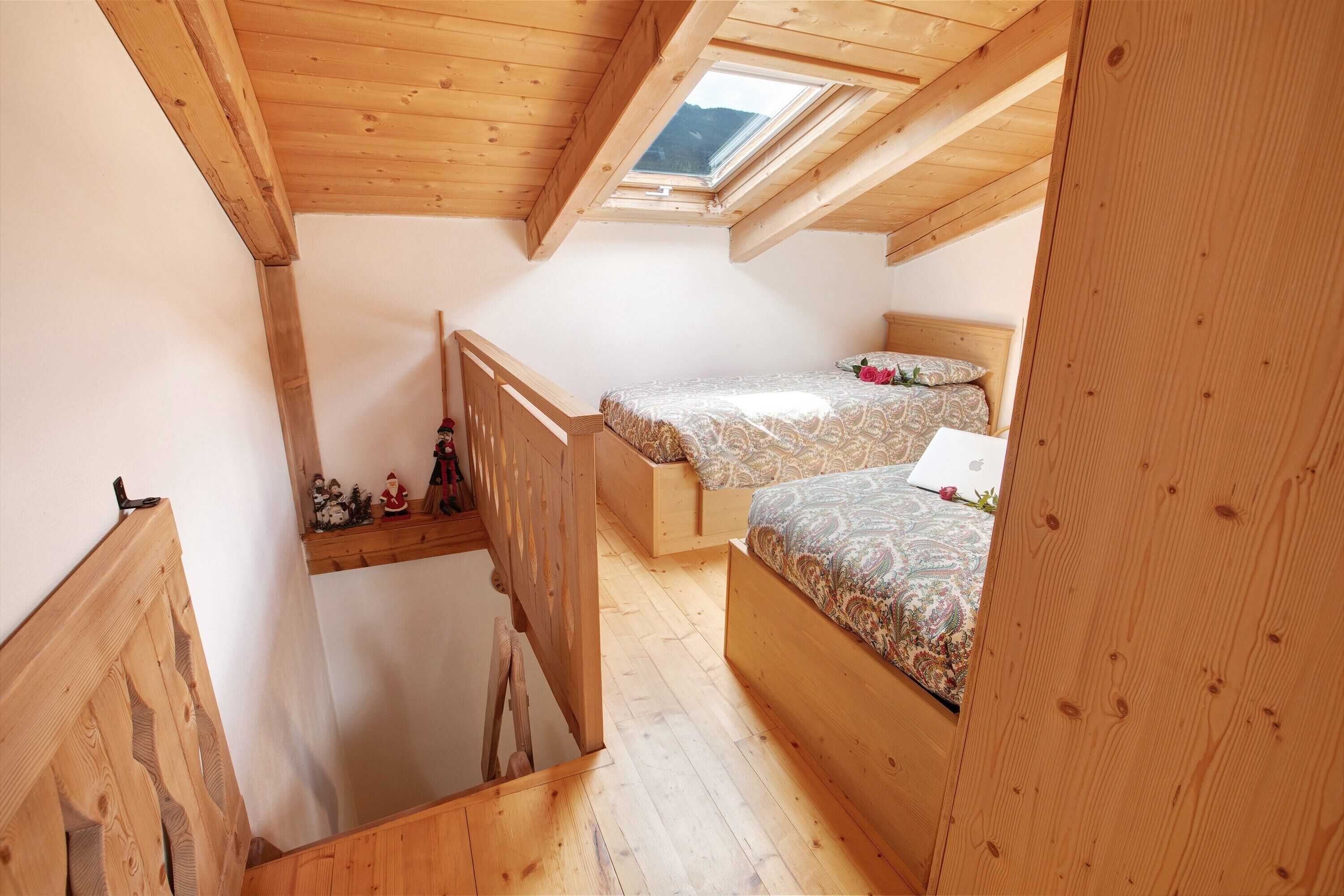 Ein kleines Schlafzimmer im Dachgeschoss mit Holzbalken, einem Oberlicht, zwei Betten und einer Holztreppe.