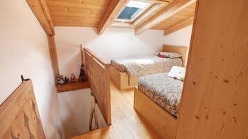 Ein kleines Schlafzimmer im Dachgeschoss mit Holzbalken, einem Oberlicht, zwei Betten und einer Holztreppe.