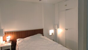 A hotel room with a bed, a desk with a lamp, a ceiling fan, and a wardrobe.