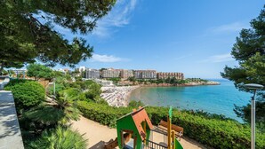 A coastal view with a beach, a playground, and a row of buildings in the background.