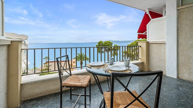 A balcony with a table set for dining, chairs, and a view of the sea.