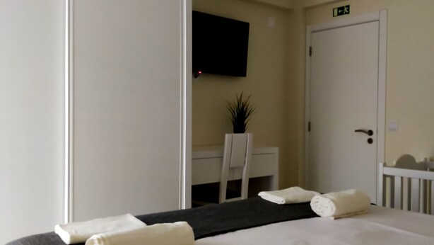 Una habitación de hotel con una cama grande, un escritorio, una silla, un televisor montado en la pared y una puerta con un cartel encima.