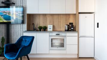 Una cocina moderna con armarios blancos, horno empotrado, cafetera y televisor mostrando una vista aérea de una ciudad.