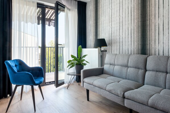 A modern living room with a grey sofa, a blue armchair, a potted plant, and a floor lamp.