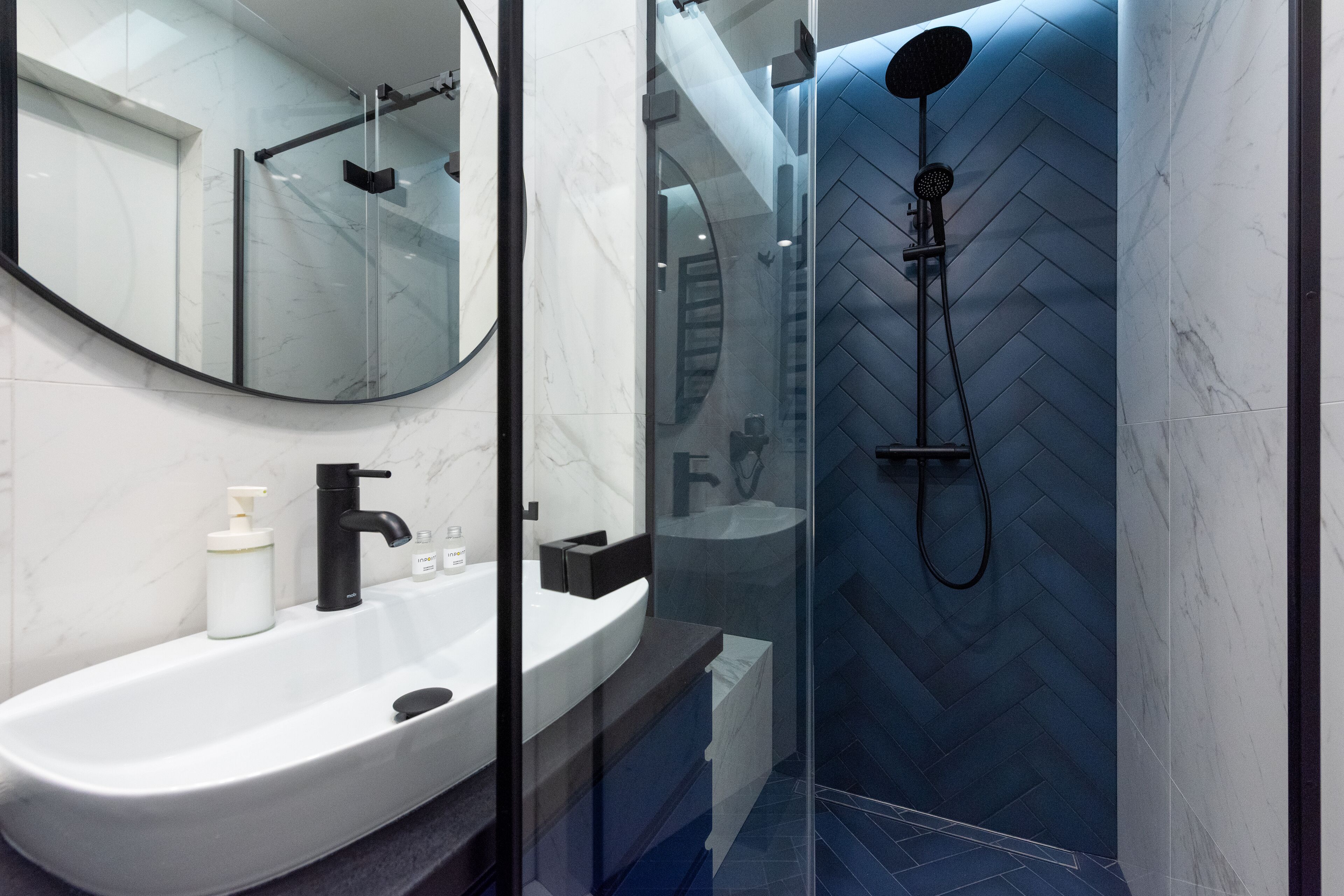 Un baño moderno con ducha de vidrio, un lavabo blanco con grifo negro y un espejo sobre el lavabo.