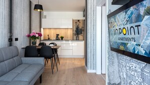 A modern apartment with a dining area, kitchen, and a large window with a cityscape view. - InPoint Cracow - Serviced Apartments G15 (Kraków)
