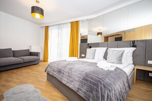A modern hotel room with a large bed, a sofa, a mirror, and a wooden floor. - InPoint Cracow - Serviced Apartments G15 (Kraków)