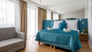 A modern bedroom with a teal bed, a grey sofa, and wooden flooring. - InPoint Cracow - Serviced Apartments G15 (Kraków)