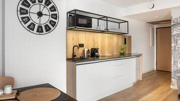 Een moderne keuken met een zwarte klok, witte kastjes, een houten aanrecht en een magnetron op een plank.