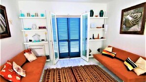 Ein Wohnzimmer mit zwei orangefarbenen Sofas, einem gemusterten Teppich und offenen Türen, die auf einen Balkon führen.