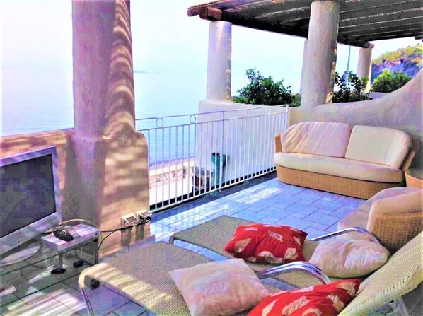 A balcony with a sofa, a chair, and a small table with a computer.