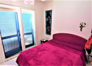 Un dormitorio con una cama grande, una puerta que da a un balcón y una mesita de noche con una lámpara.