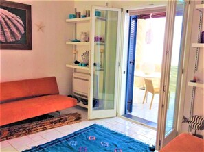 Una habitación con sofá, una puerta de cristal que da al exterior y una pequeña mesa con sillas.