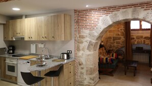 A kitchen with wooden cabinets, a granite countertop, and a stone archway leading to a living area with a sofa and a table.