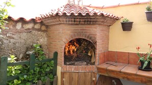 A brick outdoor oven with a tiled roof, surrounded by a wooden fence and potted plants.