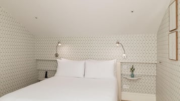 Un dormitorio con cama, dos lámparas de noche, una mesita de noche y un pequeño estante con una planta.