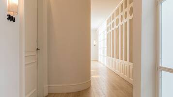 A hallway with white walls, wooden flooring, and a series of doors with decorative panels.