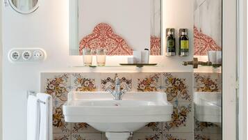 A bathroom with a white sink, a mirror, and a decorative tile backsplash. There are two bottles of lotion on the shelf above the sink.