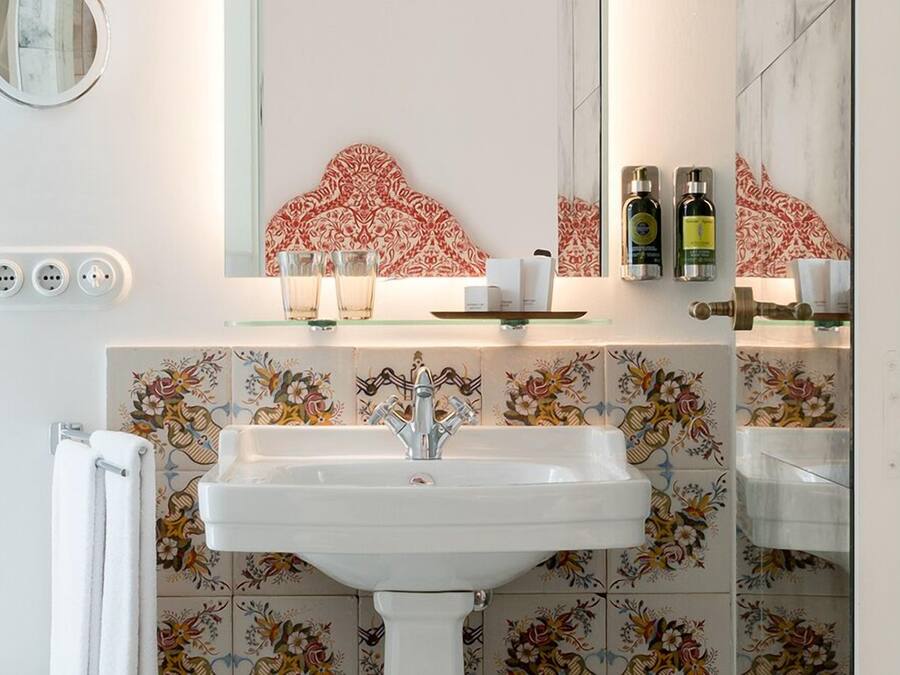 A bathroom with a white sink, a mirror, and a decorative tile backsplash. There are two bottles of lotion on the shelf above the sink.