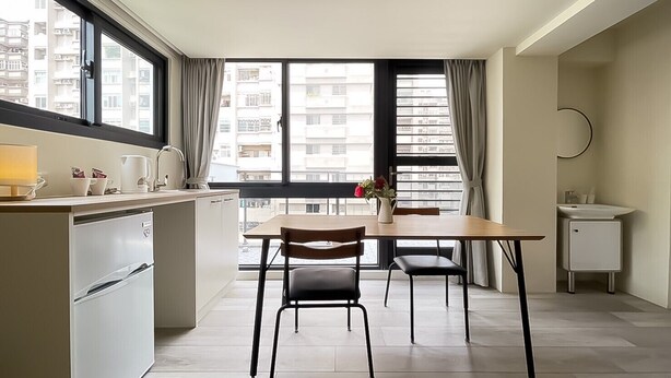 A modern kitchen with a dining area, large windows, and a view of the city. - Affetto hostel (Taichung)