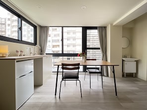 A modern kitchen with a dining area, large windows, and a view of the city. - Affetto hostel (Taichung)