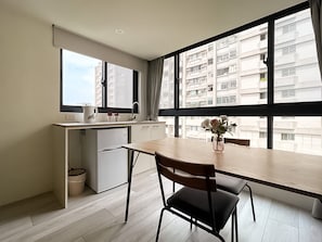 A compact kitchen with a dining area, large windows, and a view of a residential building. - Affetto hostel (Taichung)