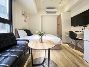 A modern hotel room with a bed, a desk, a chair, a round table, a black leather sofa, and a TV. - Affetto hostel (Taichung)