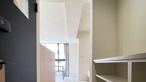 A hallway with a black door, a white shelf unit, and a view into a room with a window and curtains. - Affetto hostel (Taichung)