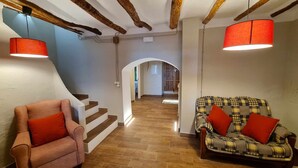 Um corredor com escadas, um sofá xadrez com almofadas vermelhas e uma poltrona rosa com uma almofada vermelha.