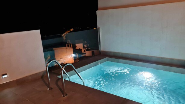 Piscina com escada de metal, rodeada por paredes azulejadas e vista para o céu noturno.