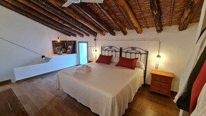 Quarto com teto de madeira, cama com almofadas vermelhas, mesa de cabeceira e luminária na parede.