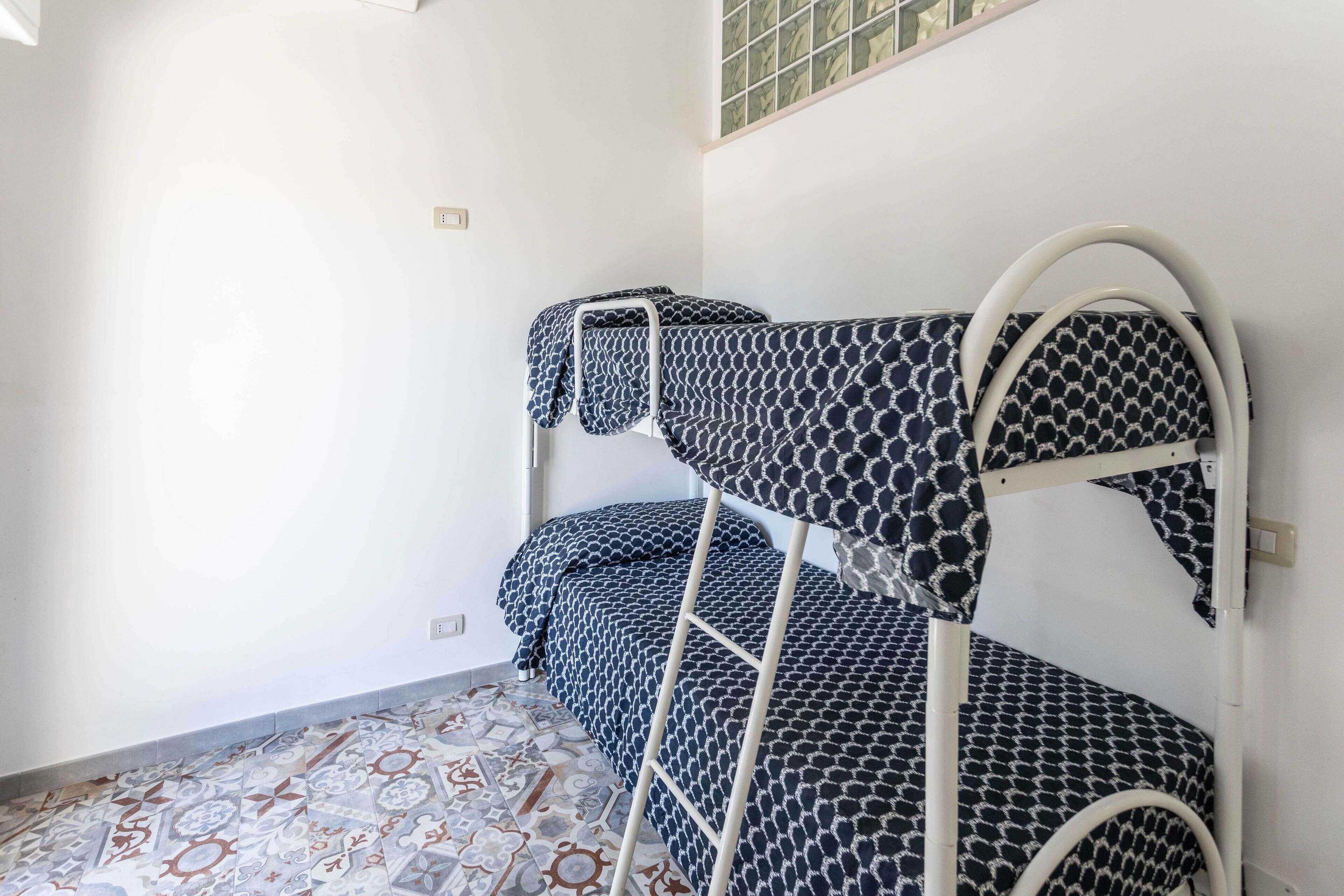 A bunk bed room with patterned bedding, a tiled floor, and a window with a view of the outside.