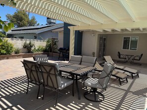 Un patio al aire libre con zona de estar cubierta, una parrilla y una vista de una casa al fondo.