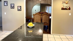 A kitchen with a marble countertop, a bowl of lemons, and a dining area with a wooden chair and table.